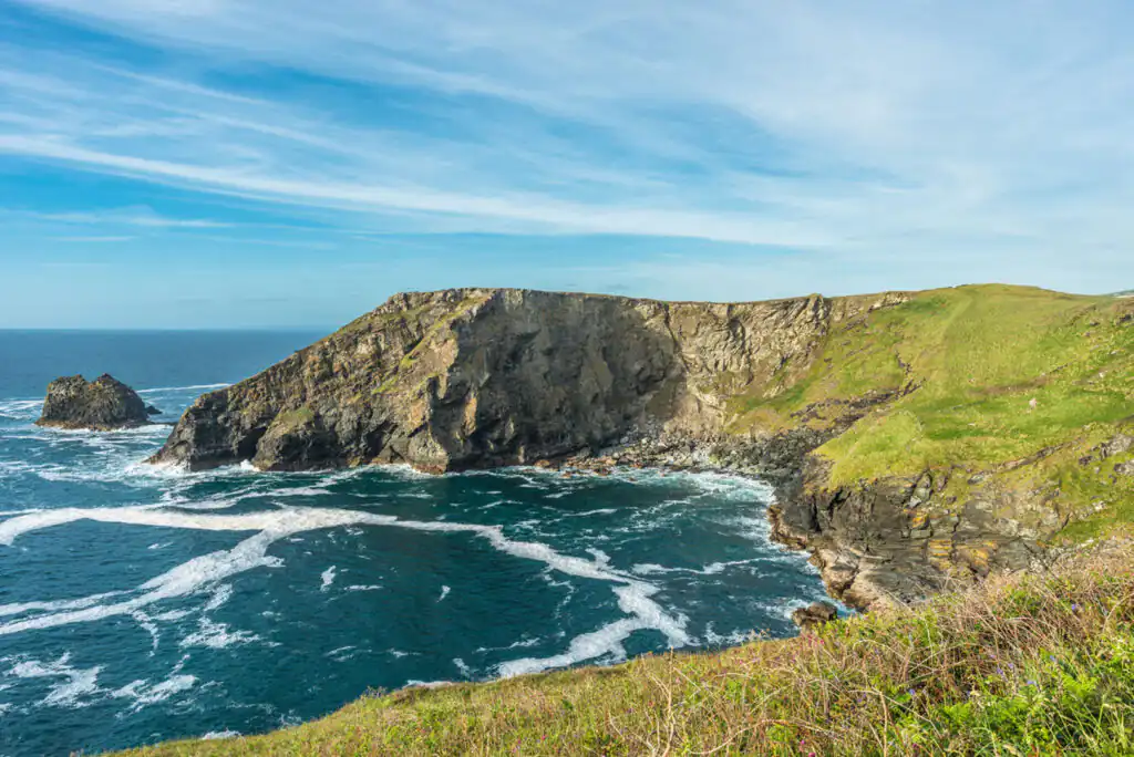 Bright blue sky with soft white clouds over Bossiney Haven, a popular swimming location near Tintagel in Cornwall.