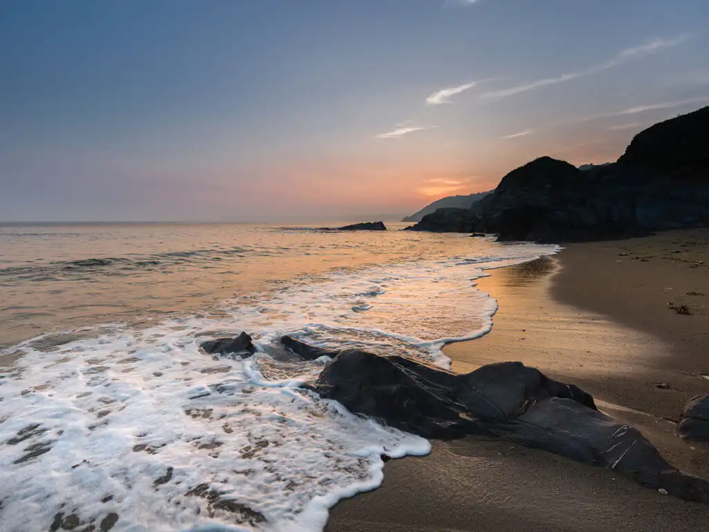 Hemmick Beach at sunset with rocky cliffs in the background.