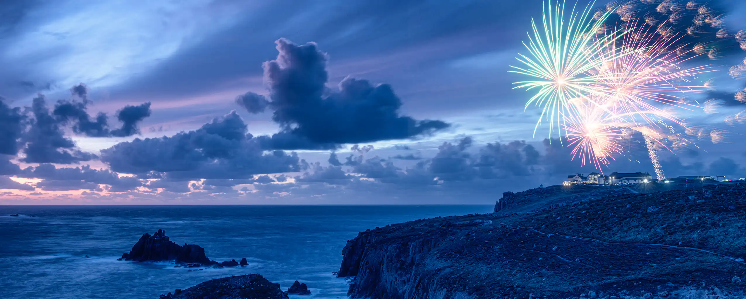 Colorful New Year fireworks illuminate the night sky over the ocean at Lands End, Cornwall, experience this event from a new year holiday cottage in Cornwall.