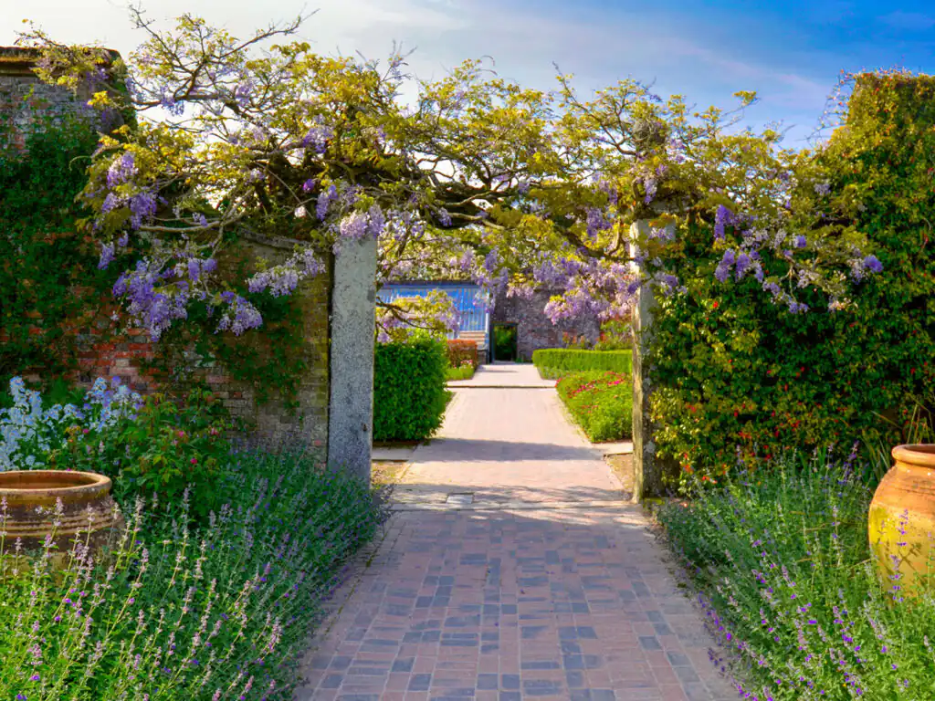 A winding brick pathway through the Lost Gardens of Heligan, surrounded by lush greenery and vibrant flowers, a vital part of Cornish Arts and Heritage.
