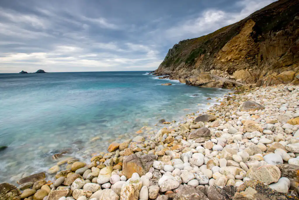 Scenic view of Porth Nanven's rocky beach, featuring calm waters in the background, ideal for swimming in Cornwall.