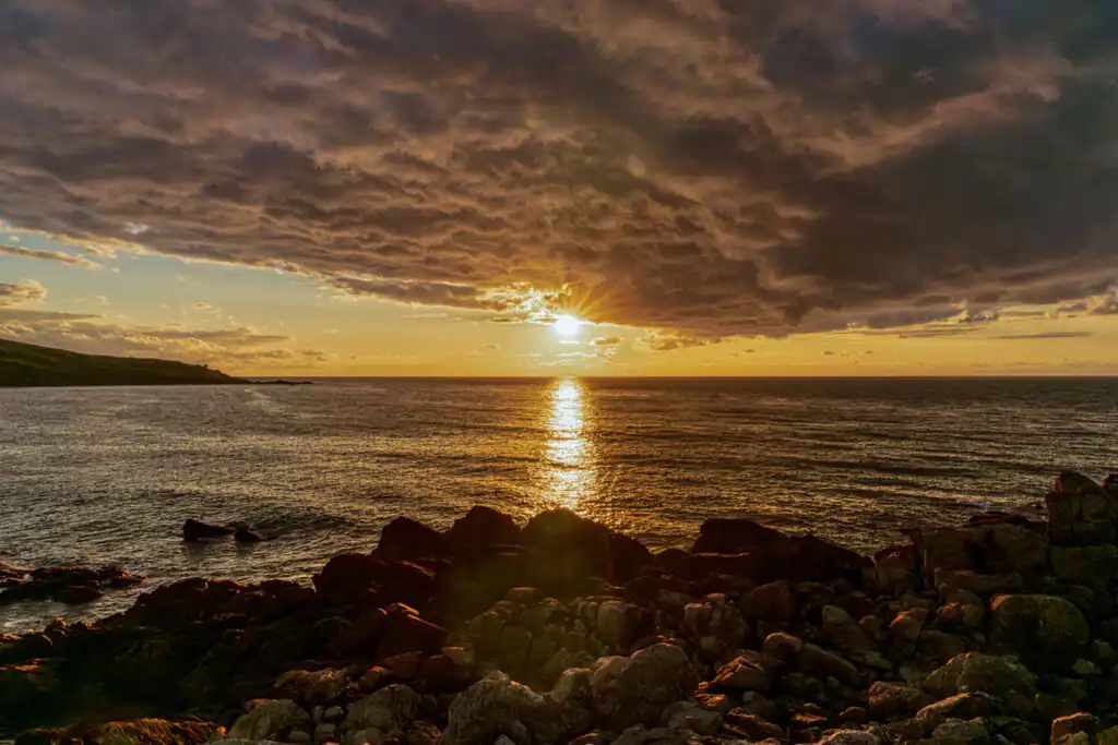 A vibrant sunset over the ocean, with coluorful clouds and rocky formations, viewed from Porthmeor Beach in St Ives.