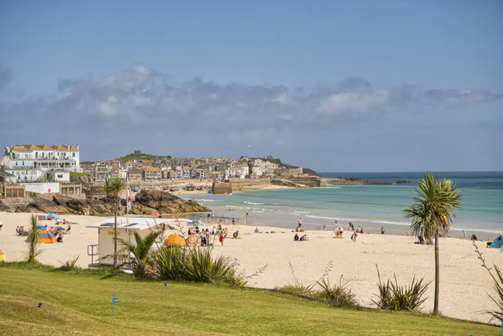 Porthminster Beach with sunbathers and swimmers, with St Ives Harbour in the distance.