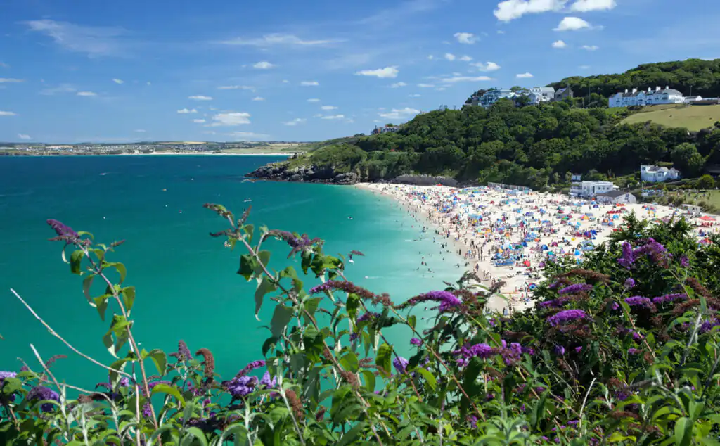 Bright blue sky with soft white clouds over Porthminster Beach, a popular swimming spot in St Ives, Cornwall.