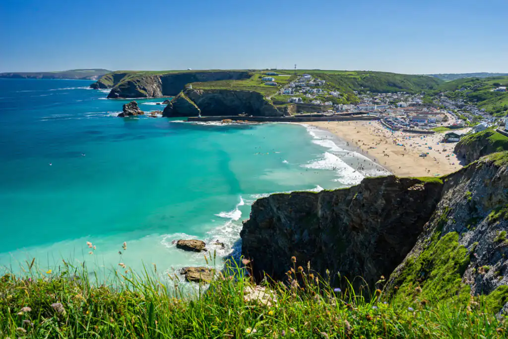 Scenic view of Portreath Beach with golden sand and lush green hillside in the background, showcasing Cornwall's beauty.