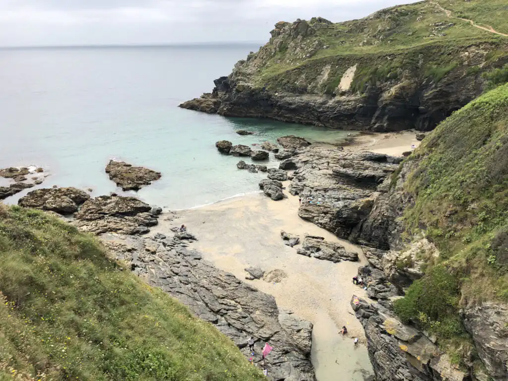 Prussia Cove showcases a rugged cliff alongside a tranquil sandy beach, perfect for swimming and relaxation.