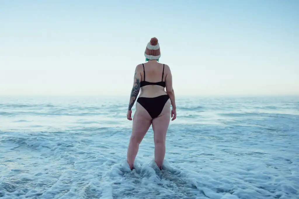 A woman joyfully stands in the ocean, celebrating the New Year while sea swimming in Cornwall.