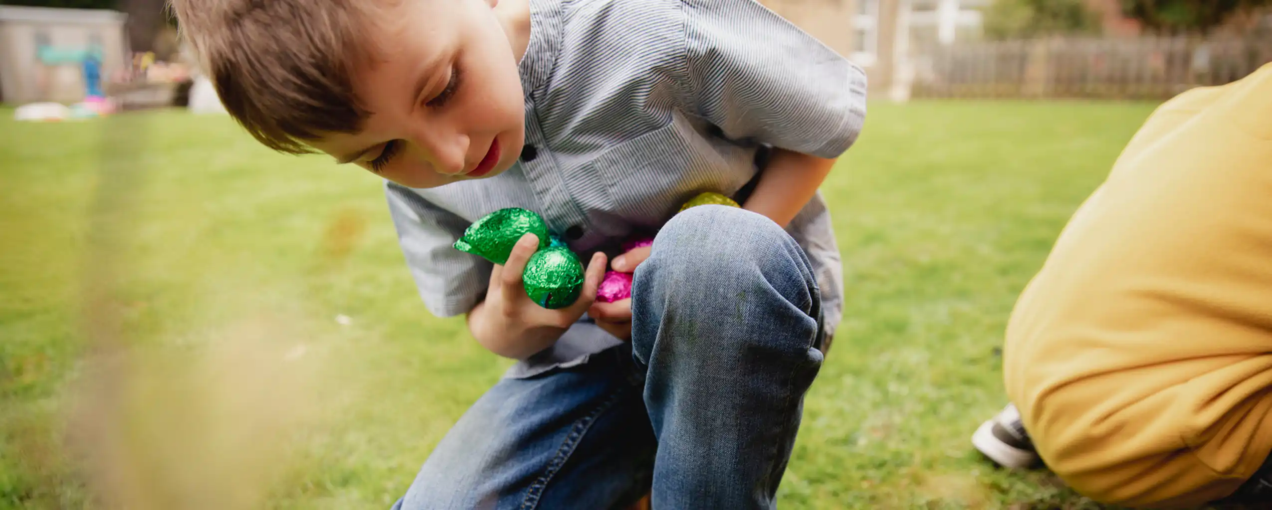 A boy joyfully holds a colourful egg while collecting Easter eggs in whilst on holiday at a Cornish Cottage at Easter.
