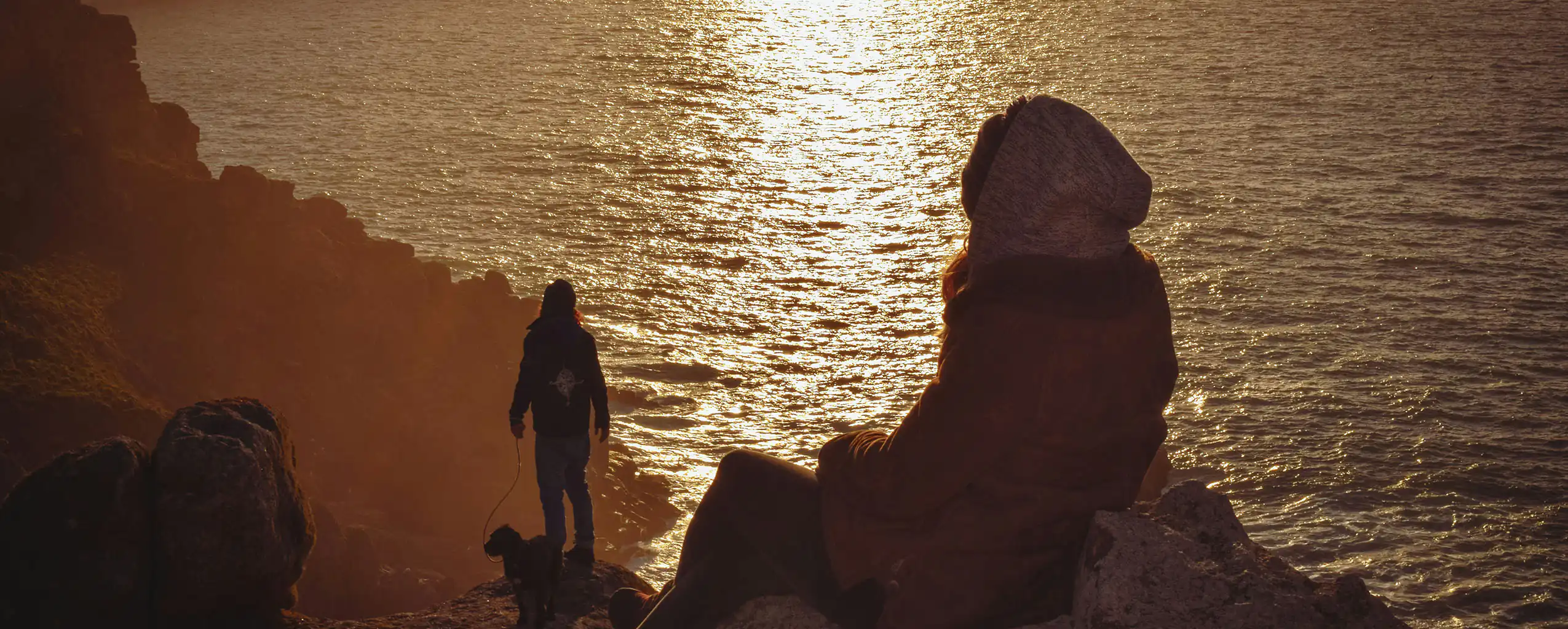A couple stands on Sennen cliffs in Cornwall, gazing out at the vast ocean below, a great place to visit from a romantic holiday cottage in Cornwall.