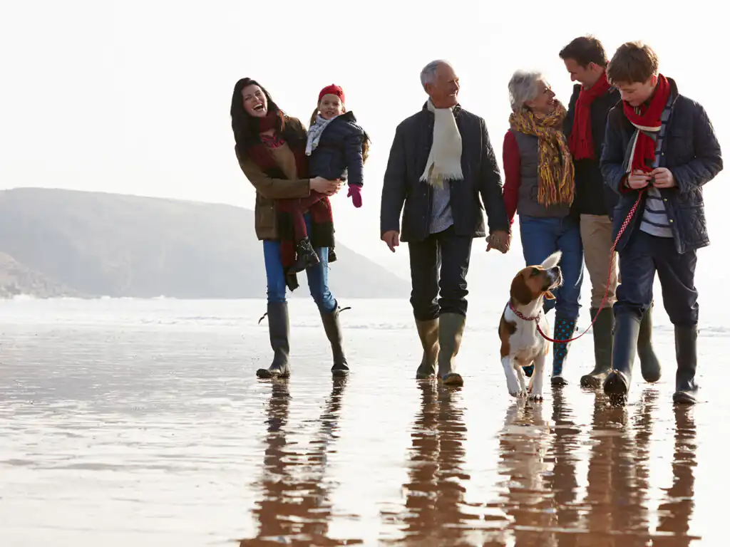 A family strolls along a Cornwall beach, enjoying the sun with their dog happily trotting beside them, a fantastic day out visiting from a large holiday cottage in Cornwall.