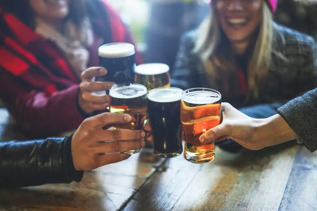 Three people joyfully toasting with beer glasses, celebrating the New Year in Cornwall, with a festive atmosphere.