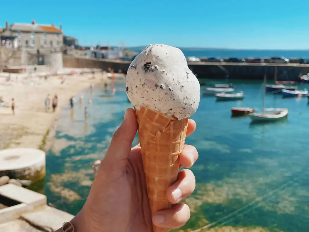 A person enjoys an ice cream cone by the water at Mousehole Harbour during a weekend break in Cornwall.