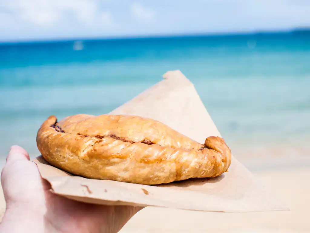 A person enjoying a pastry on St Ives Beach, with golden sand and waves in the background, on a weekend break in Cornwall.