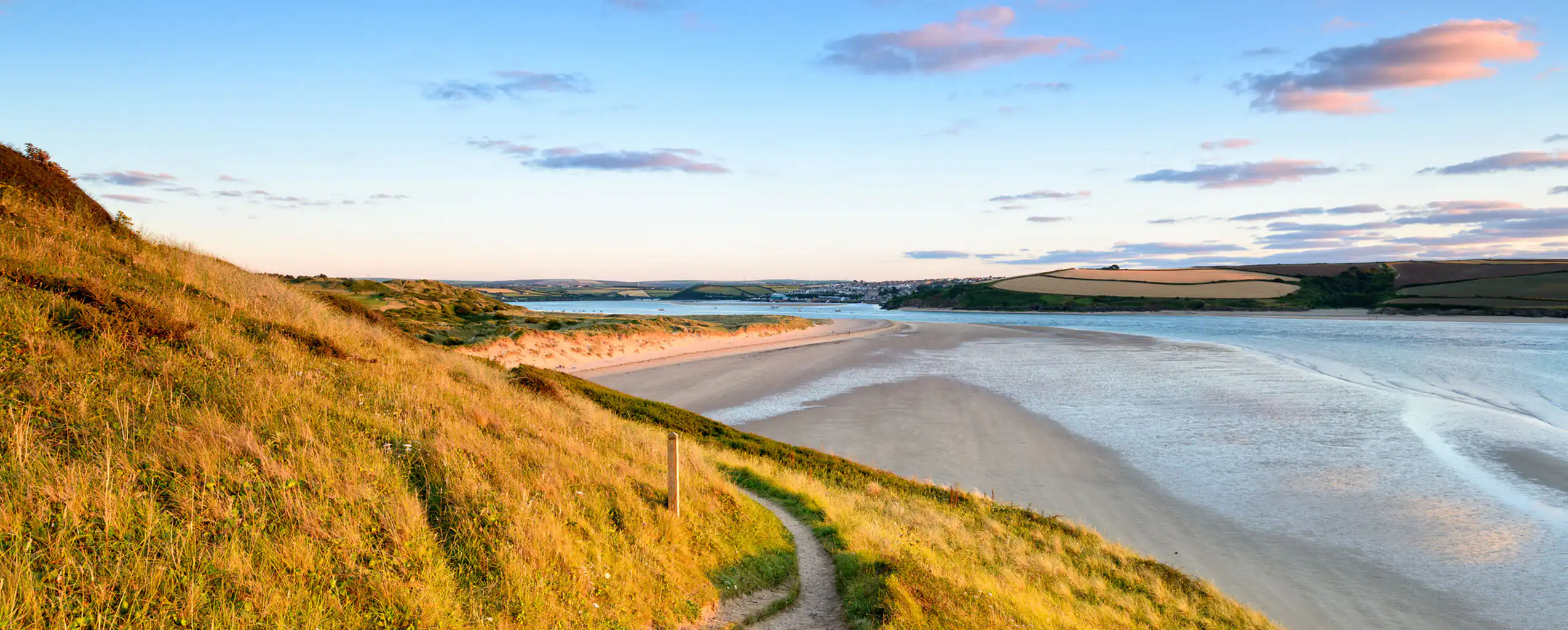 A scenic view of Camel Estuary in Cornwall, featuring a grassy beach and a path leading to the tranquil water, great to visit as a group from a Cornwall cottage sleeping 10.
