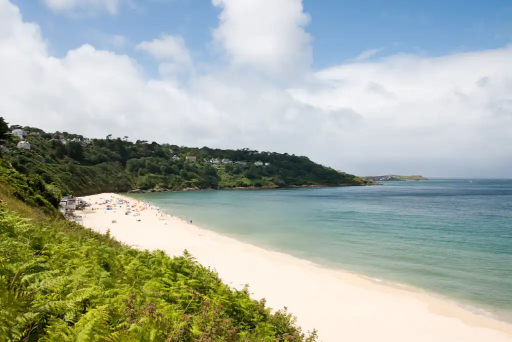 Sandy Carbis Bay Beach with lush green vegetation under a clear blue sky, perfect for a relaxing short break.