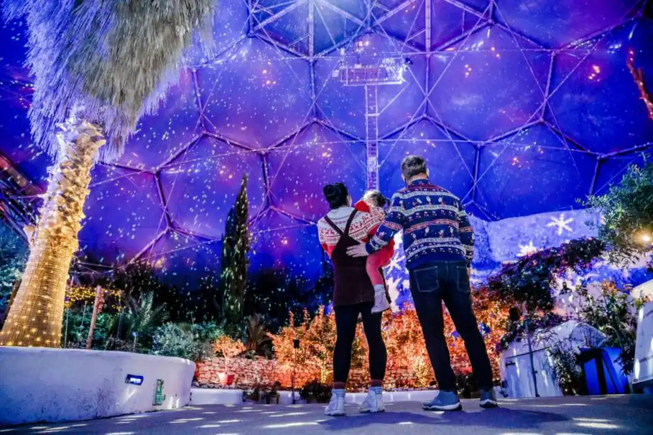 People stroll through a festive dome adorned with lights and trees at The Eden Project during Christmas.
