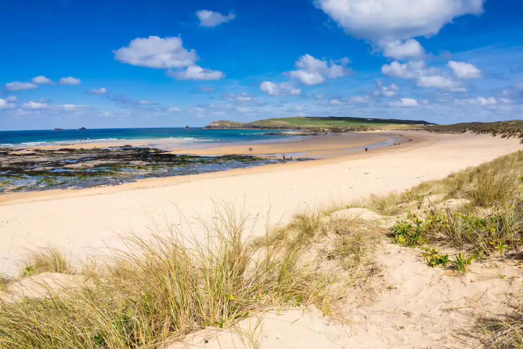 Sandy beach at Constantine Bay, a top surf spot in Cornwall, with gentle waves and golden sands under a clear blue sky.
