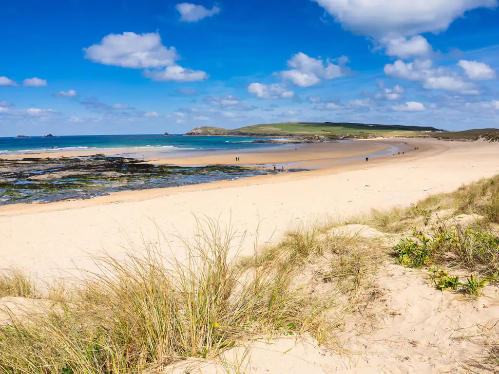 Sandy beach at Constantine Bay, with lush green grass lining the shore under a clear blue sky.