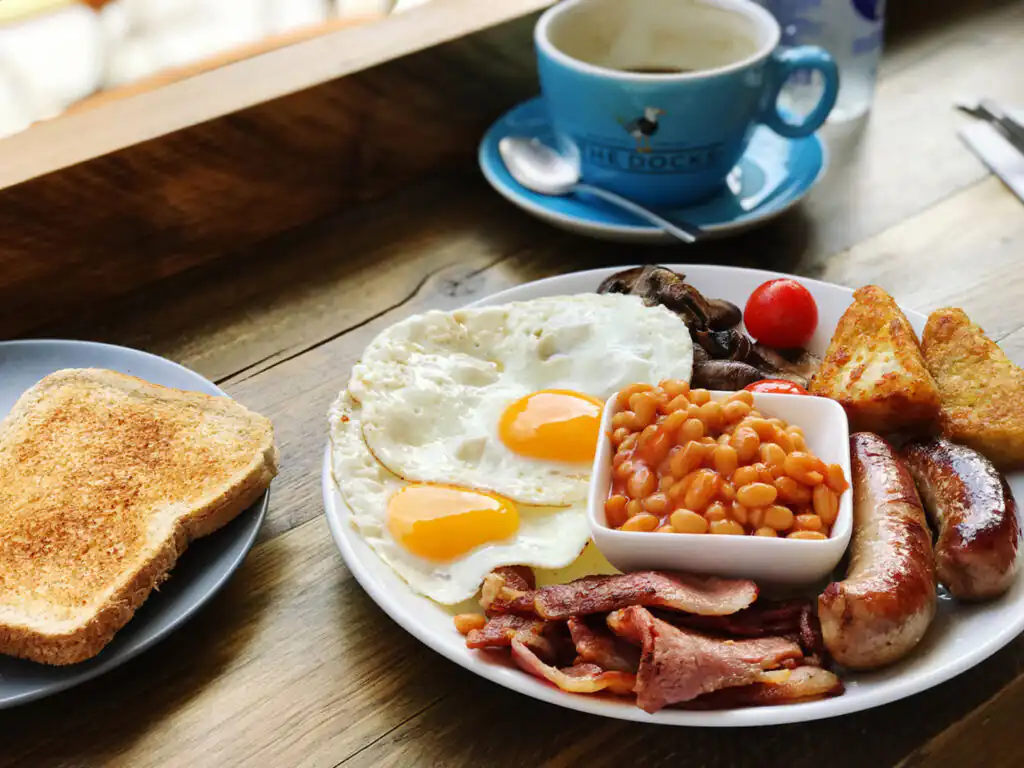 A plate of a traditional Cornish breakfast served on a table, featuring eggs, bacon, and baked beans.