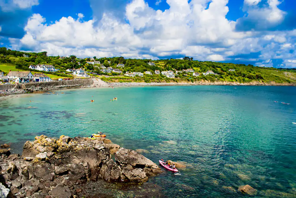 People relax on the calm waters of Coverack, a picturesque fishing village in Cornwall, surrounded by natural beauty.