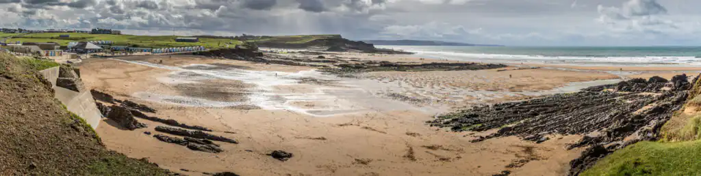 A scenic view of Crooklets Beach featuring a rocky shore and lush grassy area, perfect for surfing and relaxation.