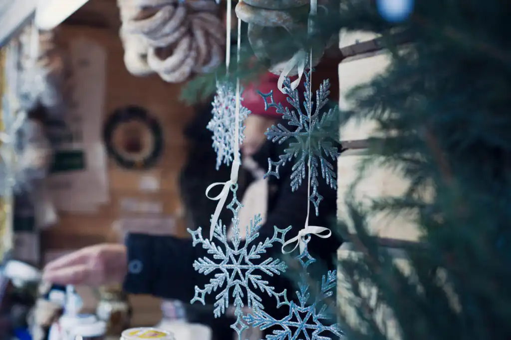 A person stands cheerfully by a decorated Christmas tree, surrounded by the festive atmosphere of the Carbis Bay Christmas Market.