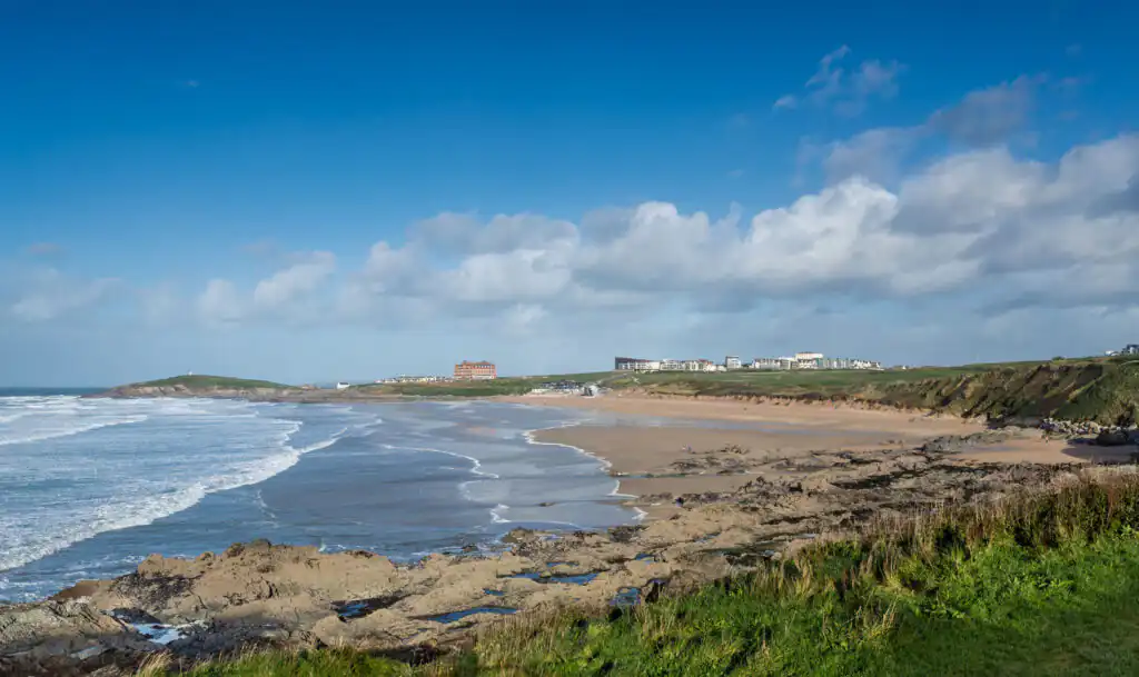 Fistral Beach in Cornwall, featuring vibrant grass and a bright blue sky, ideal for surf enthusiasts and beachgoers.