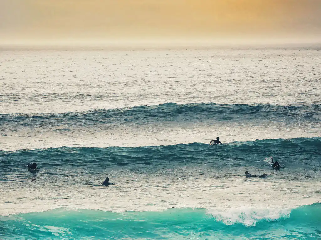 A group of surfers riding waves on surfboards at sunset in the ocean near Fistral Beach, Newquay, a great thing to do in Newequay.
