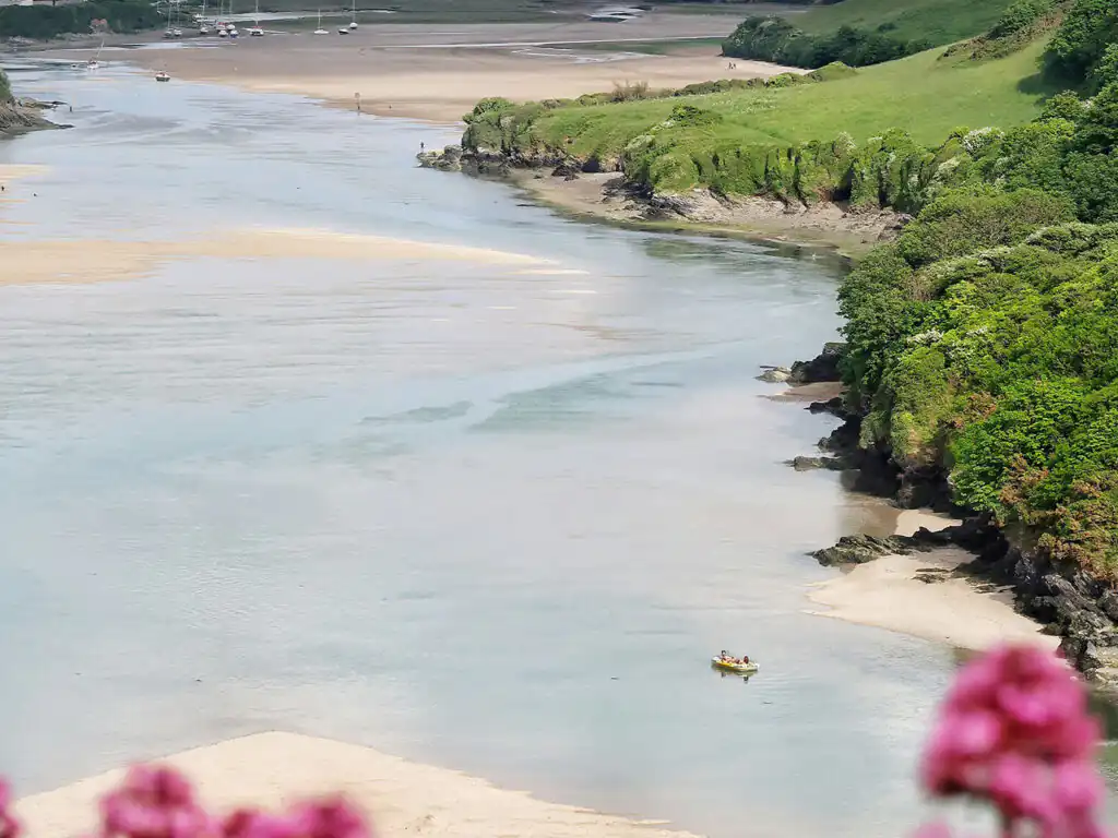 A scenic view of the Gannel Estuary in Newquay, Cornwall, featuring a boat gliding through the calm river waters.