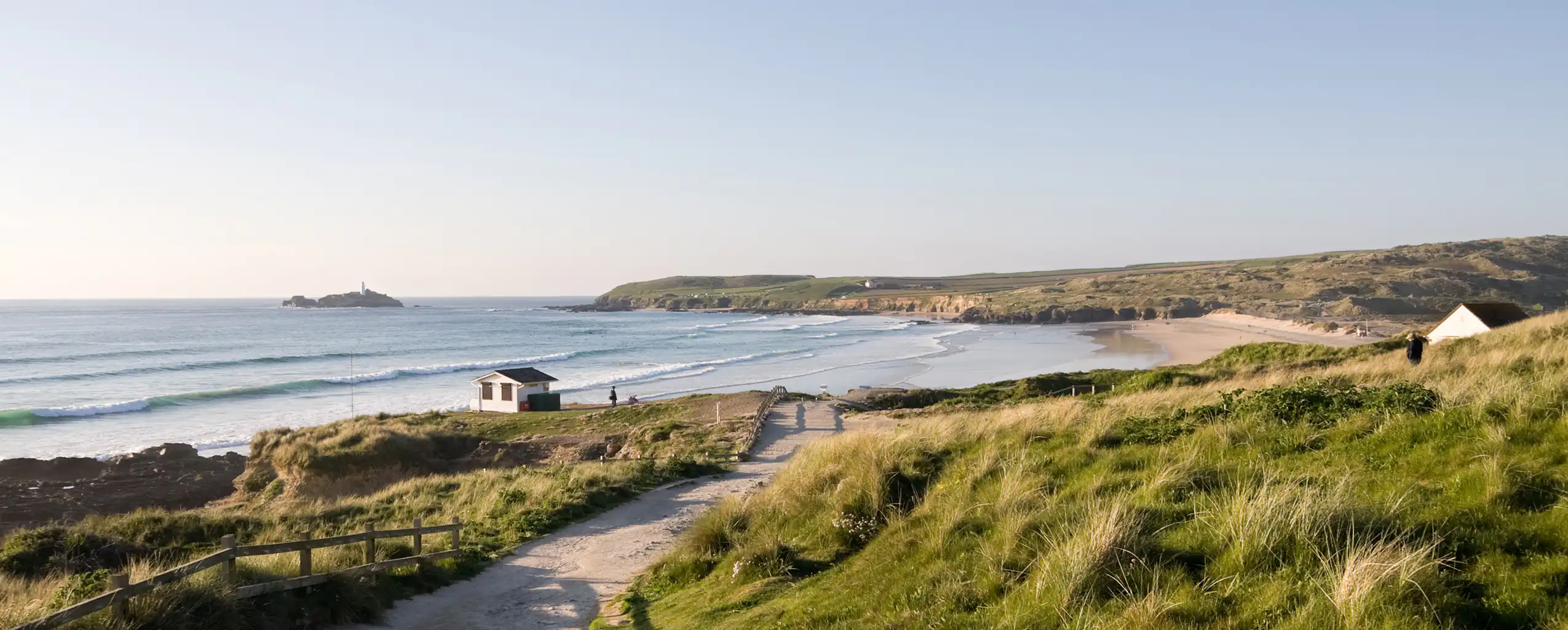 A scenic path leads to Gwithian Beach, Hayle, with a lighthouse standing tall in the background, a great holiday destination in Cornwall.