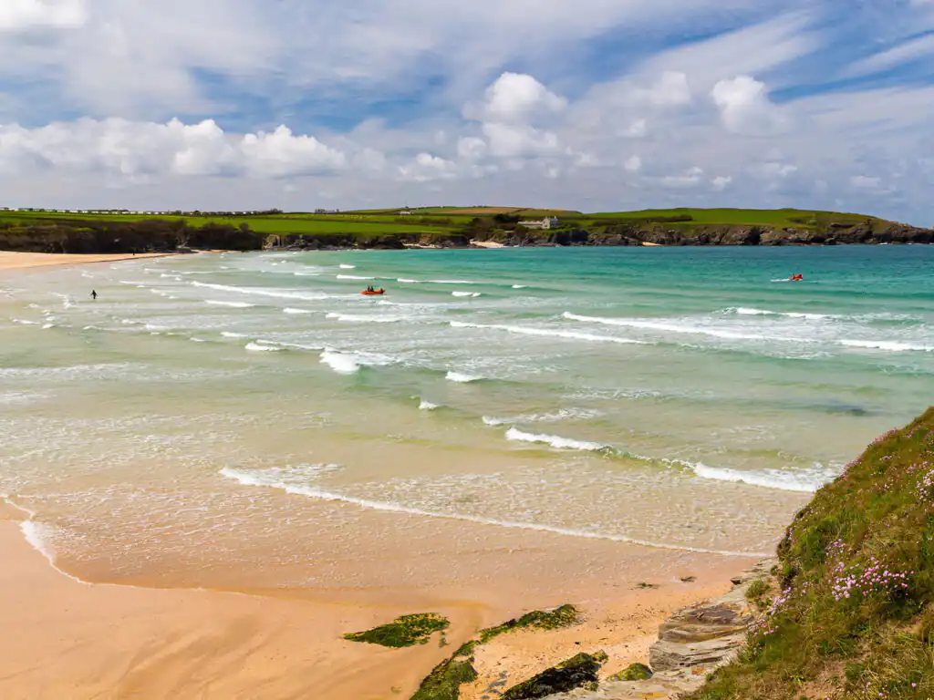 A picturesque sandy beach at Harlyn Bay, Cornwall, with gentle waves lapping at the shore under a clear blue sky.