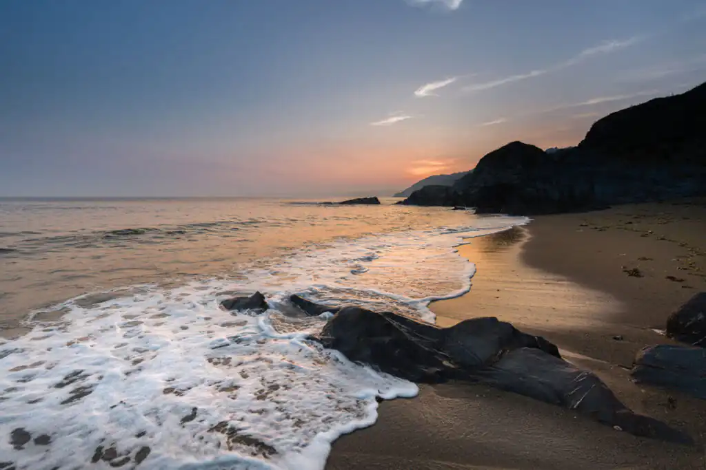 Sunset over Hemmick Beach, showcasing rocks and gentle waves, perfect for dog-friendly outings near St Austell, Cornwall.