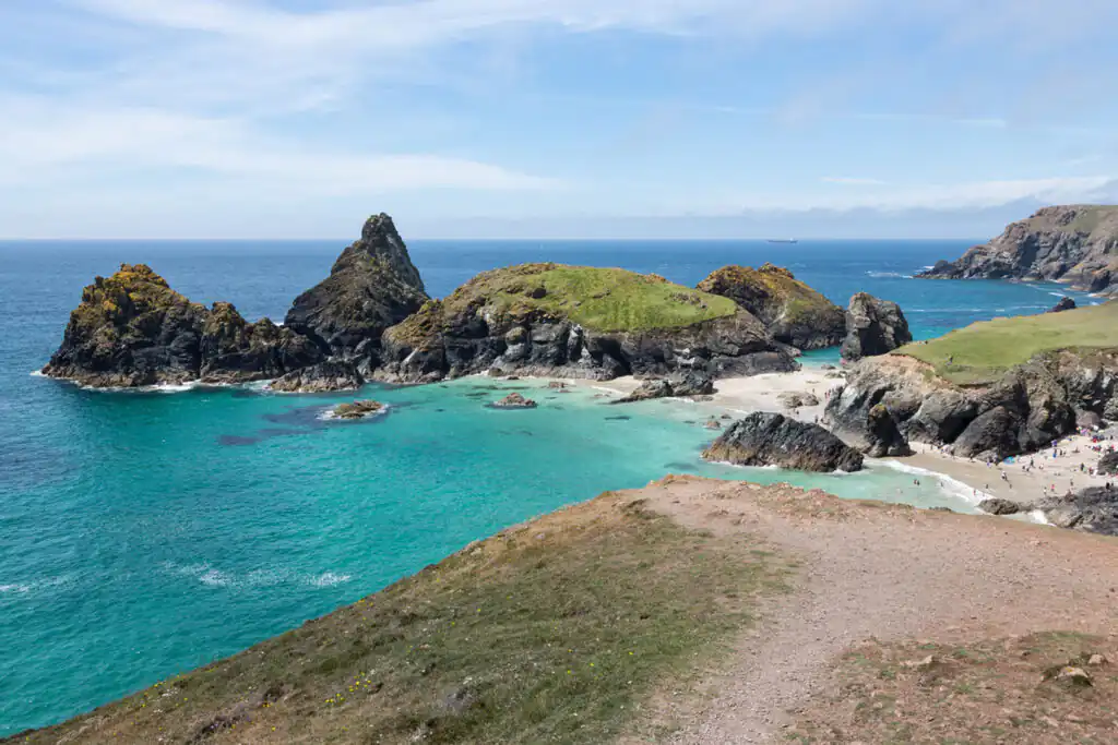 A clear blue sky dotted with fluffy white clouds over Kynance Cove, part of the National Trust in Cornwall.