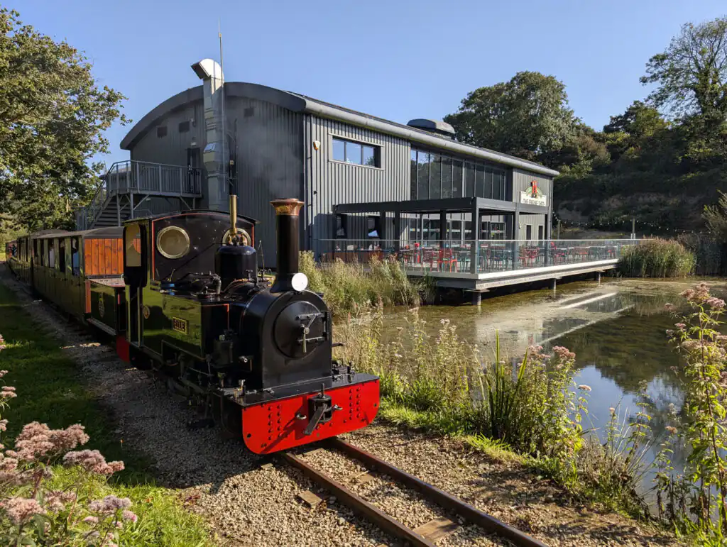 A small train travels along a track beside a building at Lappa Valley, a dog-friendly attraction in Cornwall.