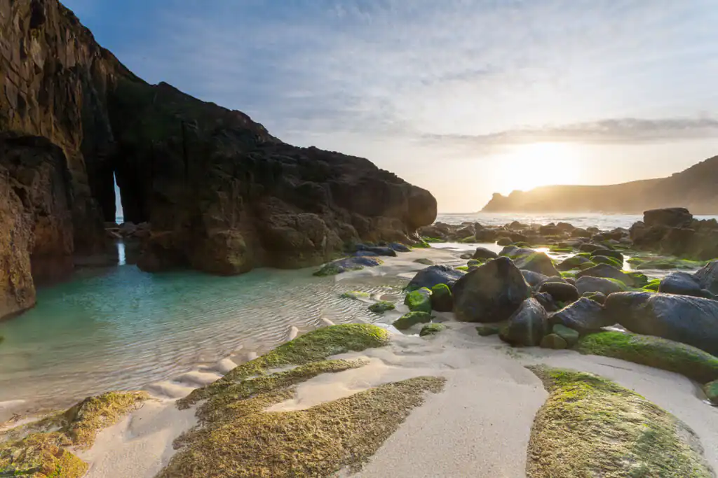 Nanjizal Beach at sunset, showcasing rocky formations and tranquil waters, ideal for a romantic evening in Cornwall.