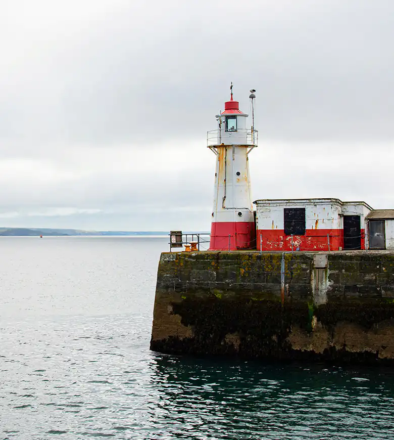 A picturesque view of Newlyn Lighthouse perched on a pier, surrounded by the tranquil waters of Mount's Bay.