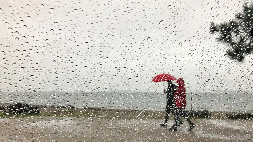 Raindrops on a window, with blurred views of St Ives and people outside holding umbrellas in the wet weather.