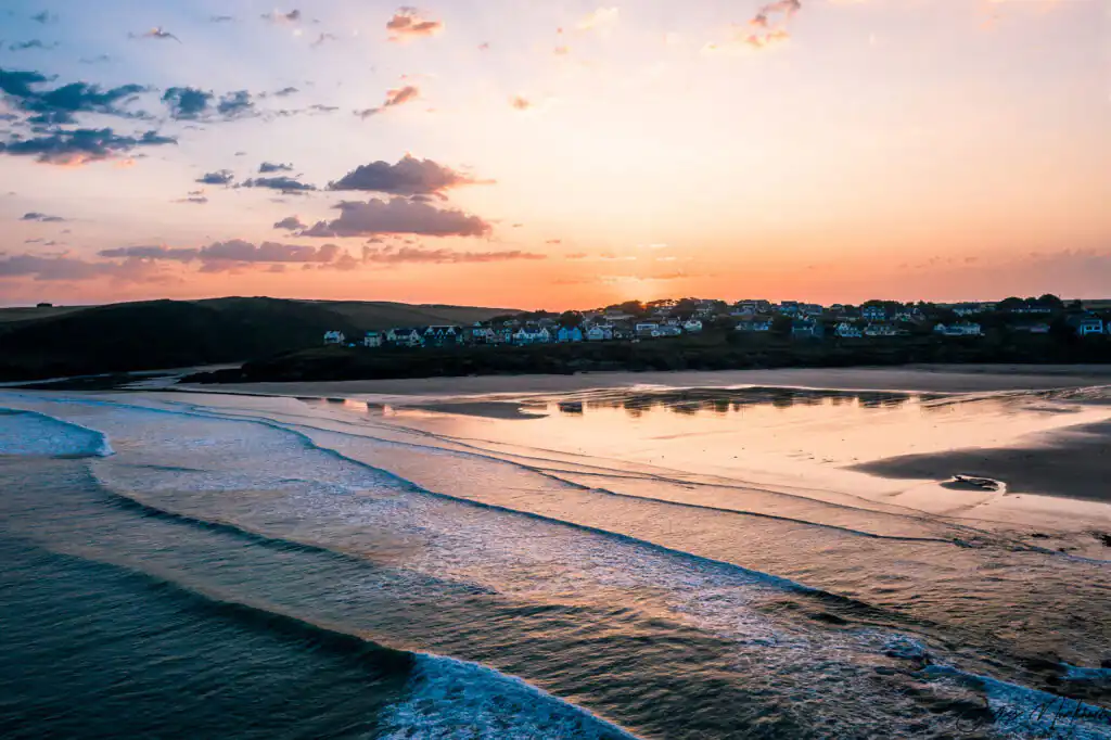 A vibrant sunset over Polzeath Beach, with gentle waves lapping at the shore, great for surfing.