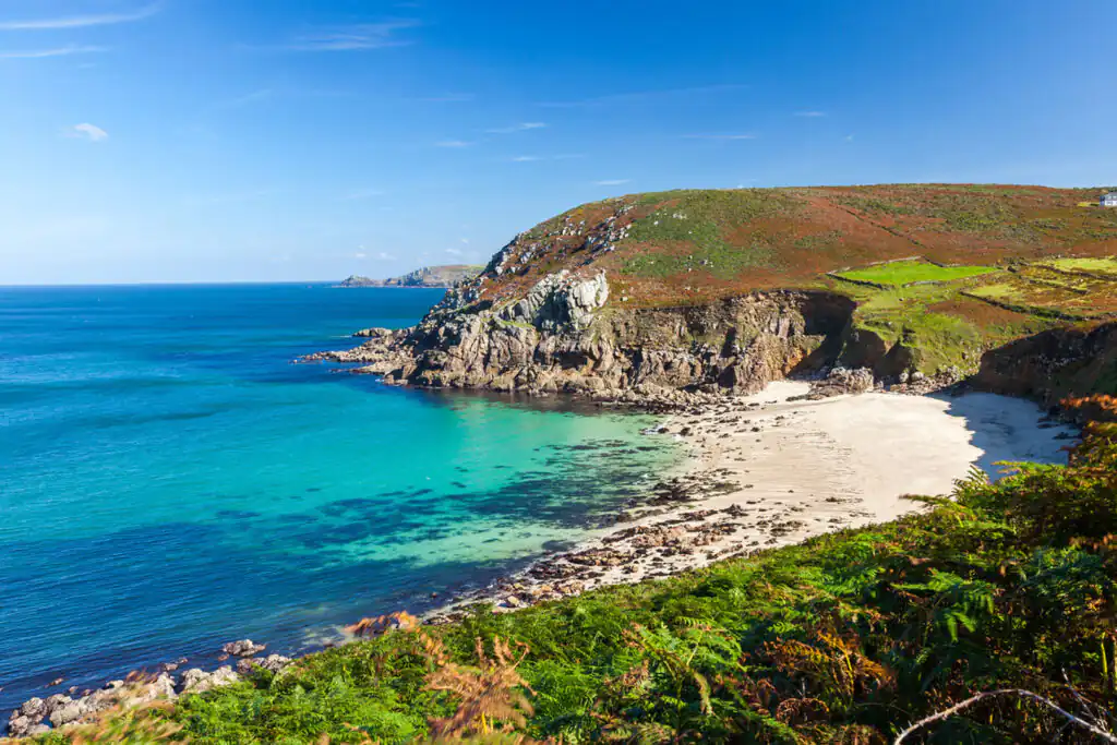 Bright blue sky with soft white clouds above Portheras Cove, a scenic dog-friendly beach near Pendeen in Cornwall.