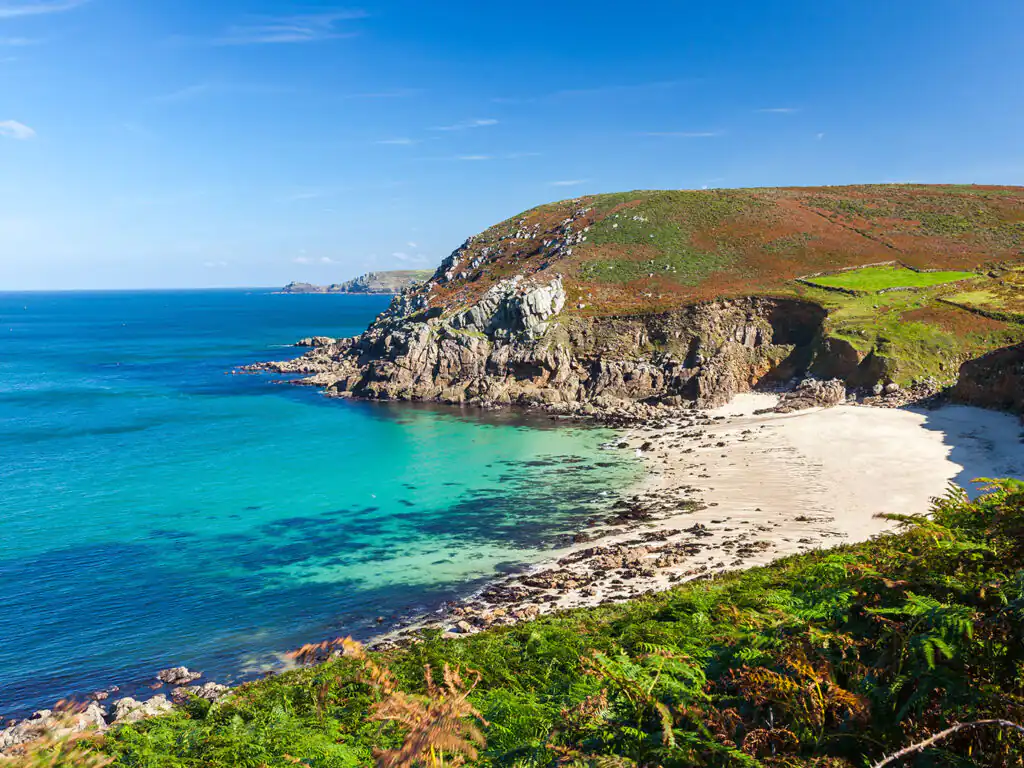 Portheras Cove in Cornwall showcases a rocky beach with a vibrant blue sky above, perfect for nature lovers.