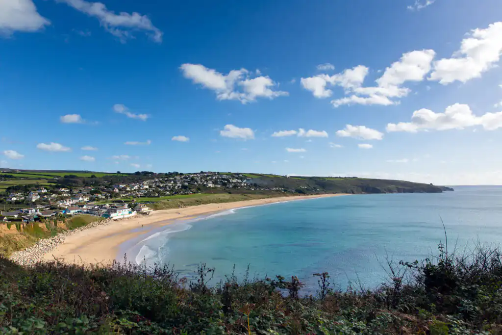 A clear blue sky dotted with fluffy white clouds over Praa Sands, a top surf spot in Cornwall.
