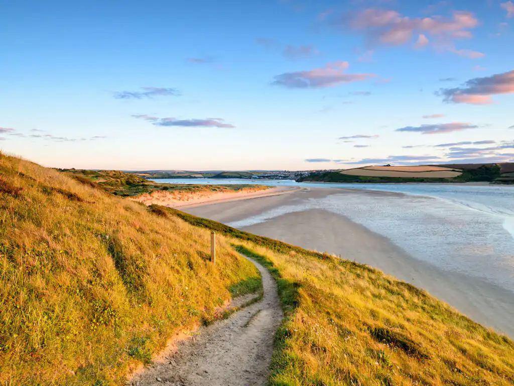 A scenic path leading to a beach at sunset, with Padstow visible across the Camel Estuary in Cornwall, a fantastic holiday destination in Cornwall.