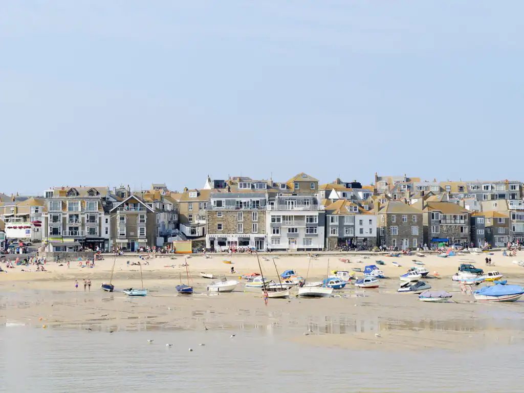 Scenic view of St Ives Harbour's sandy beach in Cornwall, dotted with boats and framed by a range of Cornwall Apartments.
