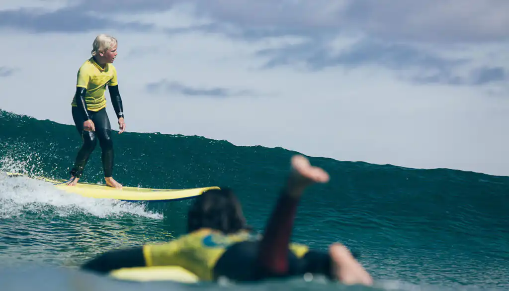 A woman balances on her surfboard, riding a wave at St Ives Surf School in Cornwall, perfect for February Half Term.