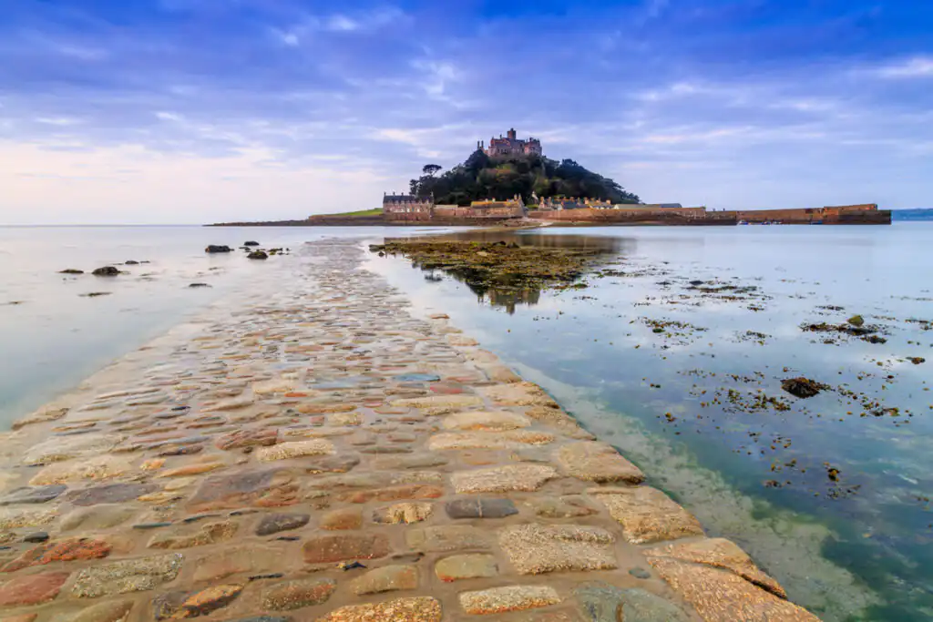A picturesque stone path leads to a castle on the water, showcasing the romantic beauty of St Michael's Mount in Cornwall.