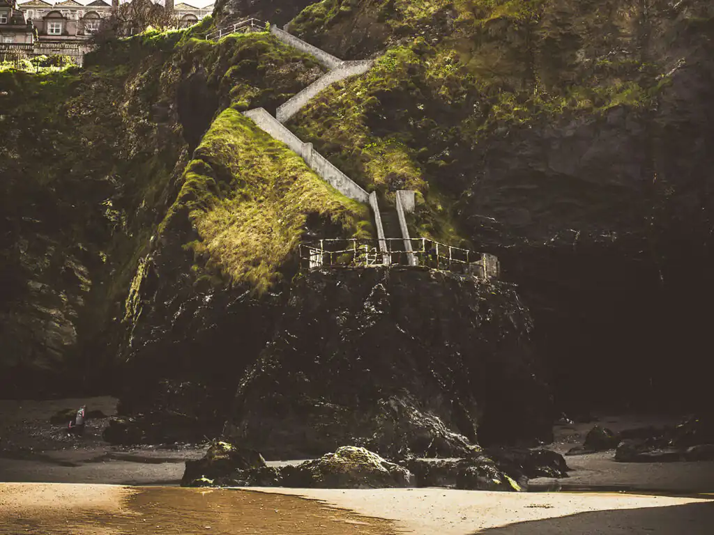 Steps leading down to Tolcarne Beach in Newquay, with a scenic cliff backdrop and sandy shoreline visible, a great activity in Newquay.
