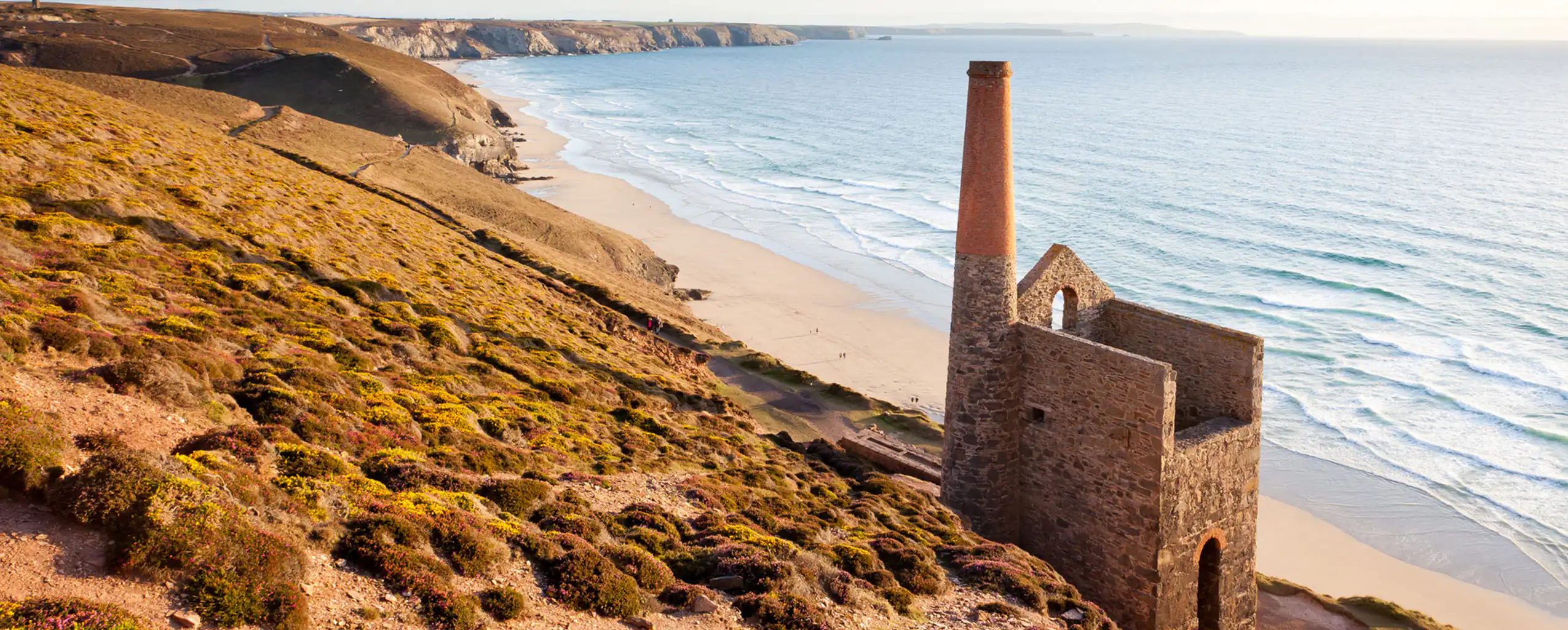 Scenic view of Towanroath Engine House on a hill overlooking a sandy beach and the ocean, near St Agnes, a great place to visit on a short break in Cornwall.