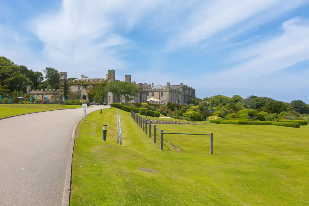 A picturesque road winds toward Tregenna Castle, with a lush grassy field behind, perfect for cream tea lovers in St Ives.