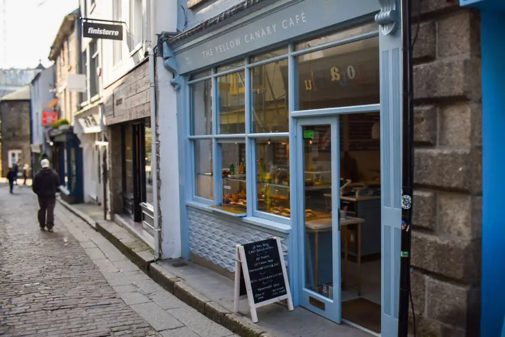 A person strolls down a street past The Yellow Canary Cafe, a great place for a Cream Tea in St Ives.
