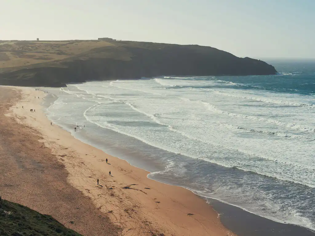 A picturesque Cornwall beach featuring calm waters and a handful of visitors relaxing under the sun, a great activity to undertake away from a cottage with sea views in Cornwall.